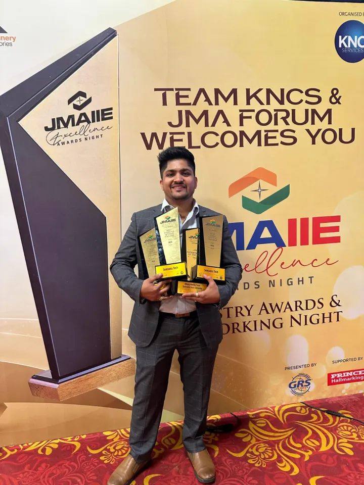 Dhyey Mehta of Semsons Tech holding the JMAIIE Excellence Awards Night trophies in front of the event backdrop